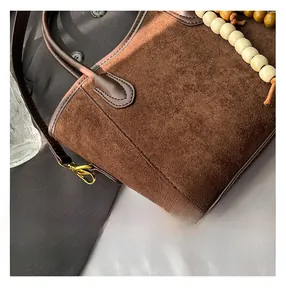 Détail du sac seau en daim marron avec finitions en cuir, dorures et perles en bois