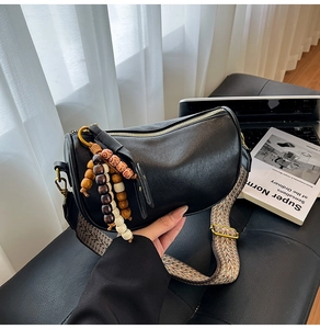 Close-up of black leather crossbody bag with woven strap and decorative beaded pendant