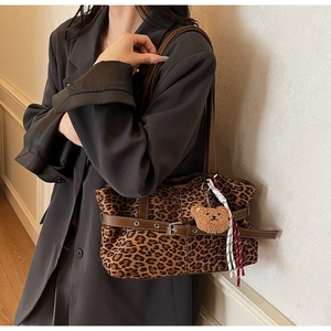 Detail of leopard print tote bag featuring brown leather straps and a plush bear charm