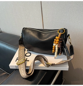 Detail of black Boston bag featuring ethnic woven wide strap and wooden bead tassel decor