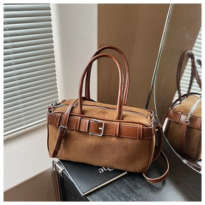 Detail of brown suede bucket bag with leather straps on a wooden table setup