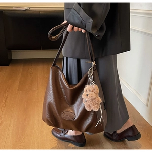 Detail view of deep brown hobo bag with Banatu logo plate and plush teddy bear charm