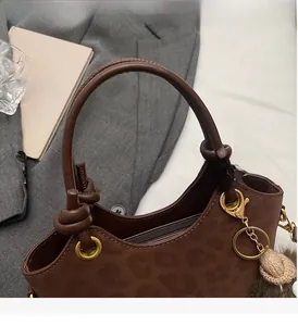 Détail du sac seau en daim marron avec motif léopard, poignée nouée et breloque pompon
