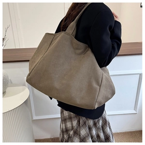 Detailed side view of large khaki suede tote bag carried by model in minimalist setting