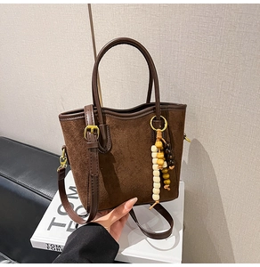 Détail du sac seau en daim avec bordures en cuir et pompon décoratif en perles de bois