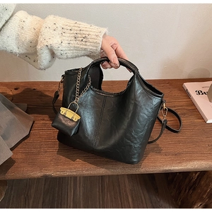 Détail d'un sac cabas noir en cuir PU texturé avec mini pochette dorée sur un banc