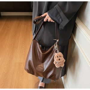 Detail view of large dark brown leather tote bag with a cute plush dog charm