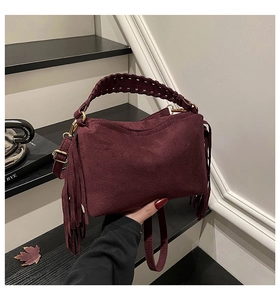 Detail of burgundy frosted leather handbag with woven handle and side tassel accents