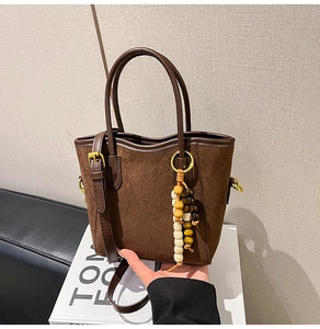 Gros plan du sac seau en daim marron avec garniture en cuir et glands décoratifs en perles de bois