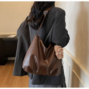 Detail view of brown leather tote with vintage texture and cute bear charm on a model