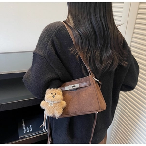 Detail view of dark brown suede shoulder bag with silver turn-lock and plush bear charm