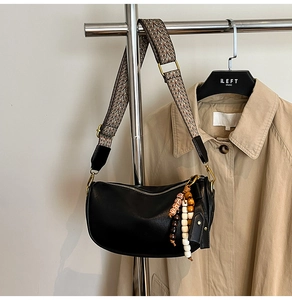 Detail of black leather crescent bag with colorful woven strap and beaded tassel
