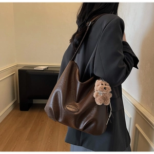 Detail of a brown leather shoulder bag with vintage texture and plush dog pendant charm