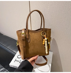 Détail d'un sac cabas en daim marron avec pendentif en perles de bois et anse en cuir
