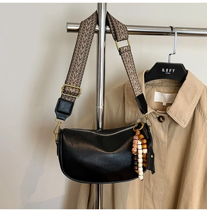 Detail of black pebbled leather crescent bag with ethnic strap and wood bead charm