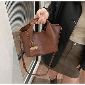 Vue détaillée du sac seau marron foncé avec chaîne dorée et pendentif en métal décoratif