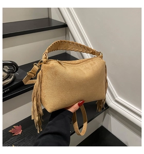 Close-up of brown suede handbag featuring fringe details and woven top handle