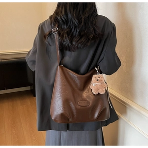 Detail of a brown PU leather hobo bag with Banatu logo and a plush bear charm on a model