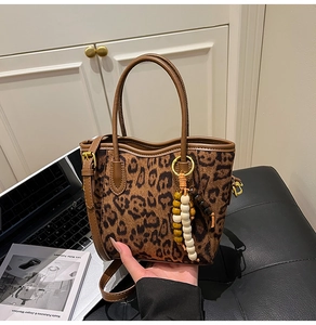 Vue détaillée du sac seau imprimé léopard avec bordure en cuir brun et breloque en bois