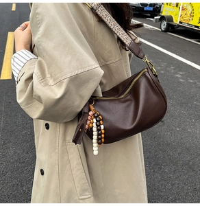 Detail of dark brown leather crossbody bag with ethnic woven strap and wooden bead tassel