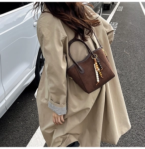 Détail du sac cabas en daim marron avec perles en bois et pompons pour la mode d'automne