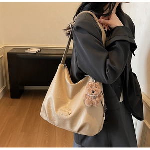 Detail of beige wrinkled texture shoulder bag featuring a teddy bear charm and logo