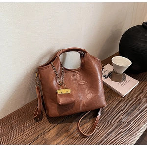 Gros plan d'un sac seau en cuir marron sur bureau en bois avec mini pochette chaîne