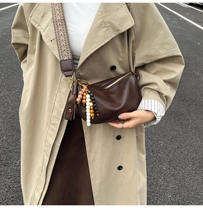 Detail of dark brown crescent crossbody bag with ethnic woven strap and bead charm