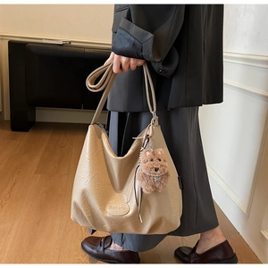 Close-up of beige hobo bag with pleated texture and plush bear charm for daily commute