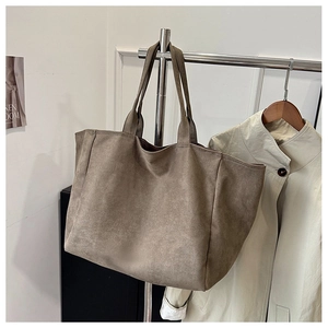 Detail of taupe suede tote bag with dual handles showing rich texture in a minimal showroom