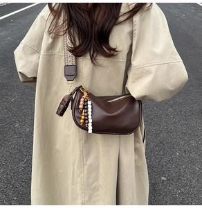 Close-up of brown crescent crossbody bag with patterned wide strap and beaded tassel detail