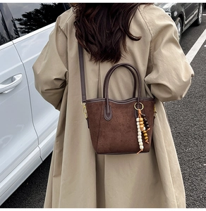 Détail du sac seau marron mat avec breloque perlée porté par un mannequin en trench