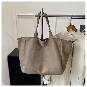 Detailed view of the dark khaki suede tote bag hanging next to a light trench coat