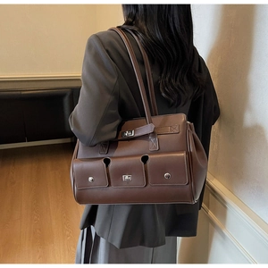 Detail of a dark brown multi-pocket shoulder bag with silver turn-lock and rivets