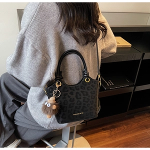 Detail of minimalist leopard print bucket bag with plush charm and shoulder strap