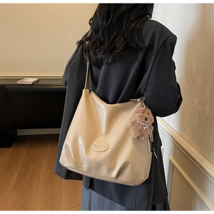 Detail showing the creamy beige pleated leather tote bag with a cute bear charm accessory
