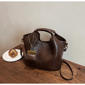 Détail du cabas en cuir marron foncé avec chaîne dorée et mini pochette assortie sur bois