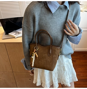 Détail d'un sac seau en daim marron avec pendentif en perles et bandoulière