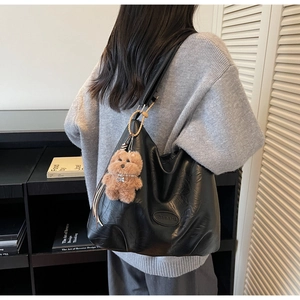 Detail of black leather tote bag with embossed logo and cute brown plush bear charm