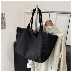 Close-up of black suede tote bag hanging on a metal rack showing its matte texture
