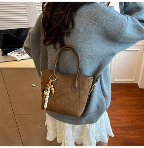Sac cabas en daim marron avec pendentif en perles présenté dans un décor intérieur
