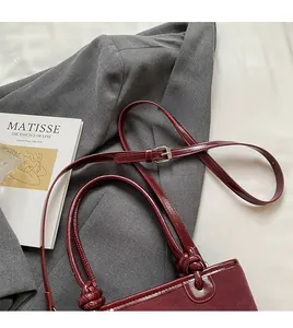 Detail of burgundy leather bucket bag with knot handle and adjustable strap on a grey suit