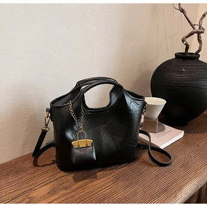 Détail du sac seau noir en cuir PU brillant avec chaîne métallique et mini pochette décorative