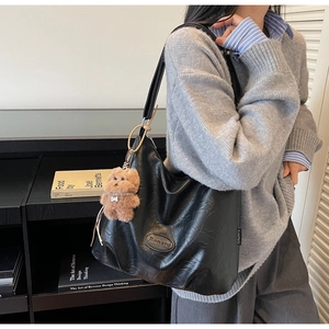 Detail of black large tote bag featuring pleated texture and cute brown bear pendant charm