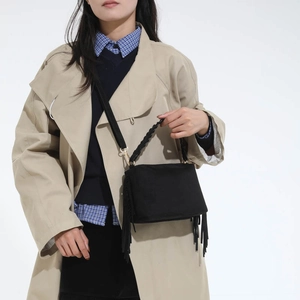 Detail of black suede satchel with fringe tassels and woven rope handle on beige trench coat