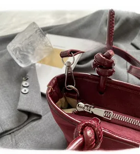 Detailed close-up of wine red bucket bag showing silver zipper and knotted handle strap
