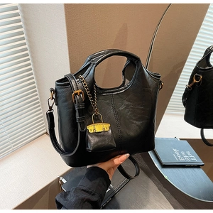 Détail du sac seau en cuir texturé noir avec poignée ronde et breloque mini sac