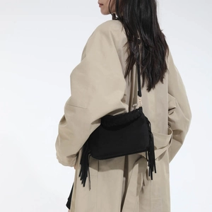 Close-up of black suede crossbody bag featuring long bohemian tassels and metal hooks