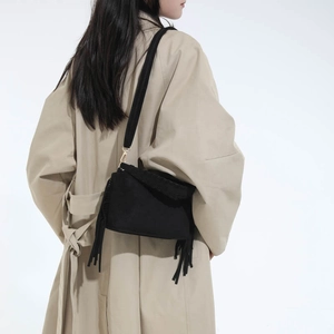Detail of a black suede crossbody bag with long tassels on a light trench coat