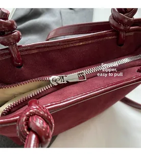 Close-up of the smooth silver zipper and knotted handle design on the burgundy bucket bag
